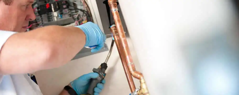 Water heater repair technician testing copper pipe connections and controls in Anaheim, CA